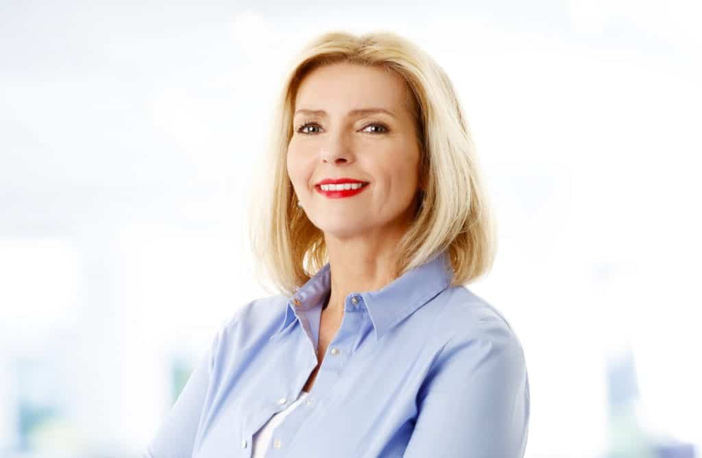 Close-up image of attractive senior woman standing at room while looking at camera and smiling.